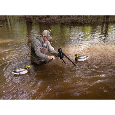 The Higdon Outdoors Motion Machine, a black tripod device with three angled legs and wire attachments, lies on the ground—an ideal water motion tool for boosting your decoy spread—shown against a white background.
